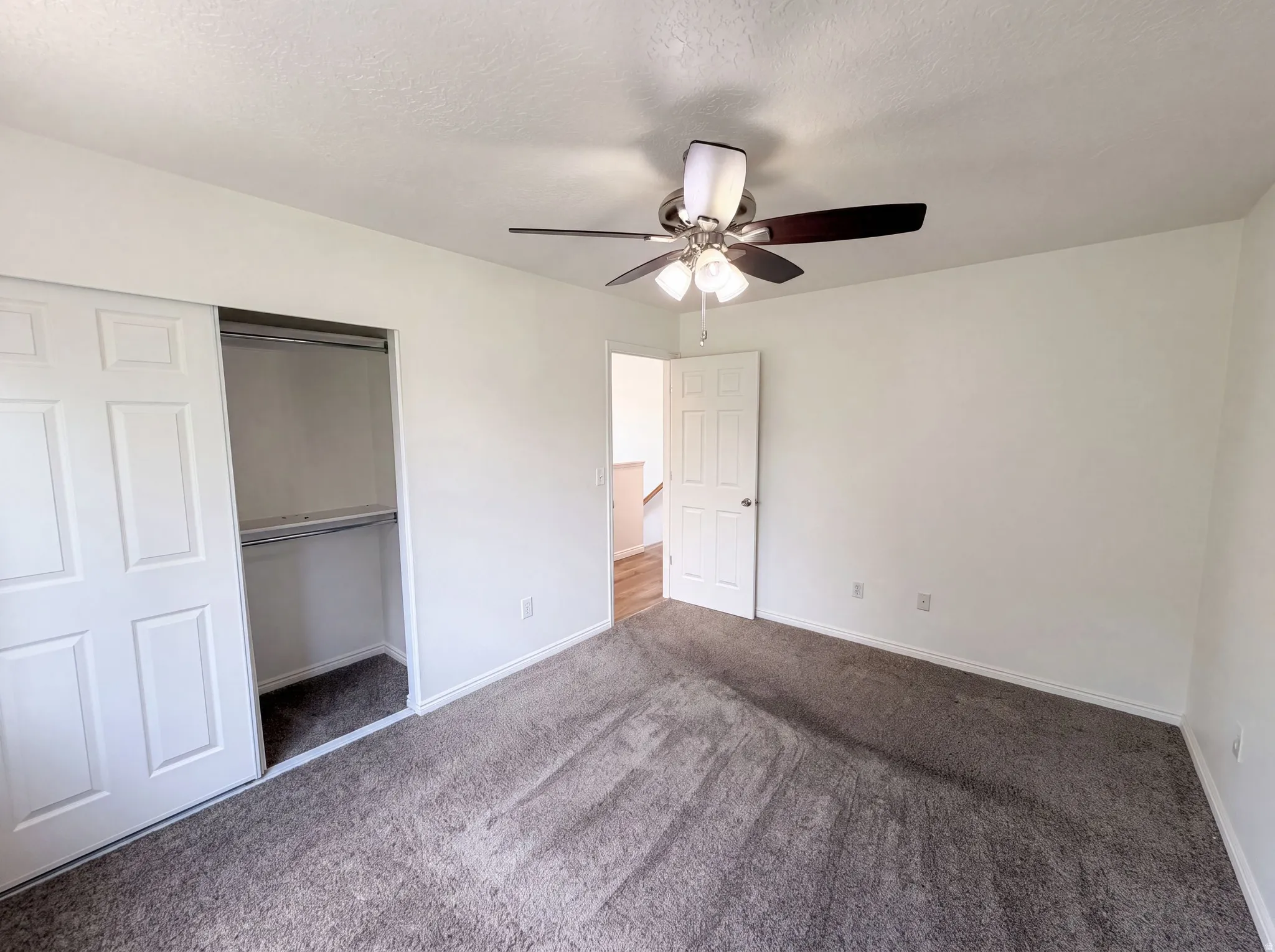 Spacious bedroom featuring neutral carpeting, ceiling fan with integrated lighting, and direct access to an adjoining room