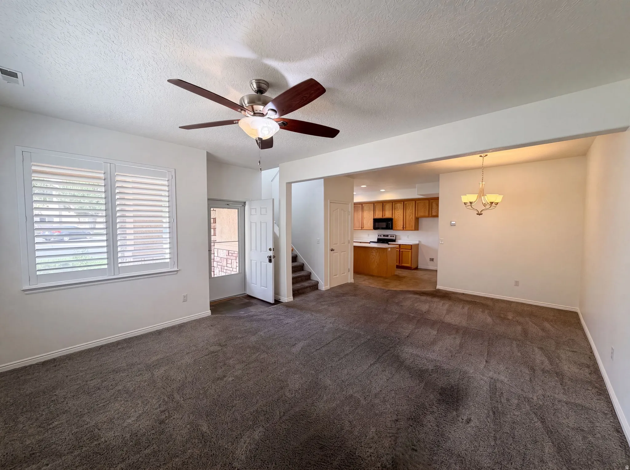 Spacious living area featuring neutral carpeting, a ceiling fan with integrated lighting, and plantation shutters