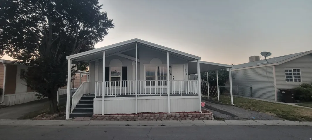 Single-story residence featuring a covered front porch with white railing, exterior siding, and a paved driveway leading to a covered carport