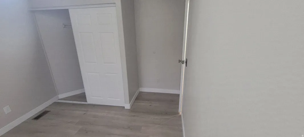 Light gray walls complement the wood-finish flooring in this room featuring a closet with a bi-fold door and an additional entry