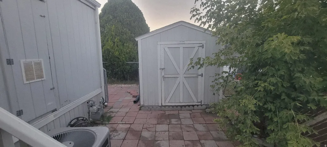 Storage shed with a pitched roof and double barn doors, set on a red paver patio