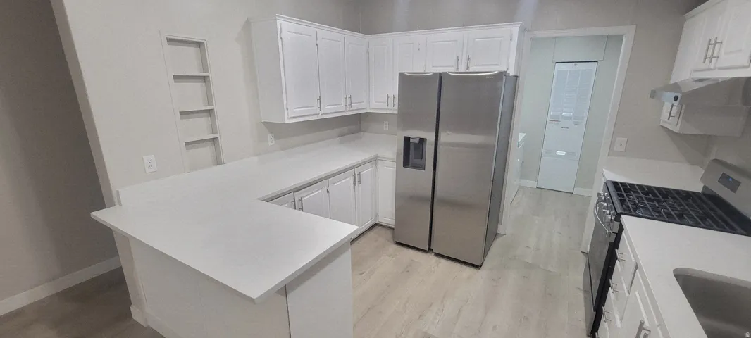 Modern kitchen featuring white cabinetry, light countertops, stainless steel appliances, and wood-finish flooring