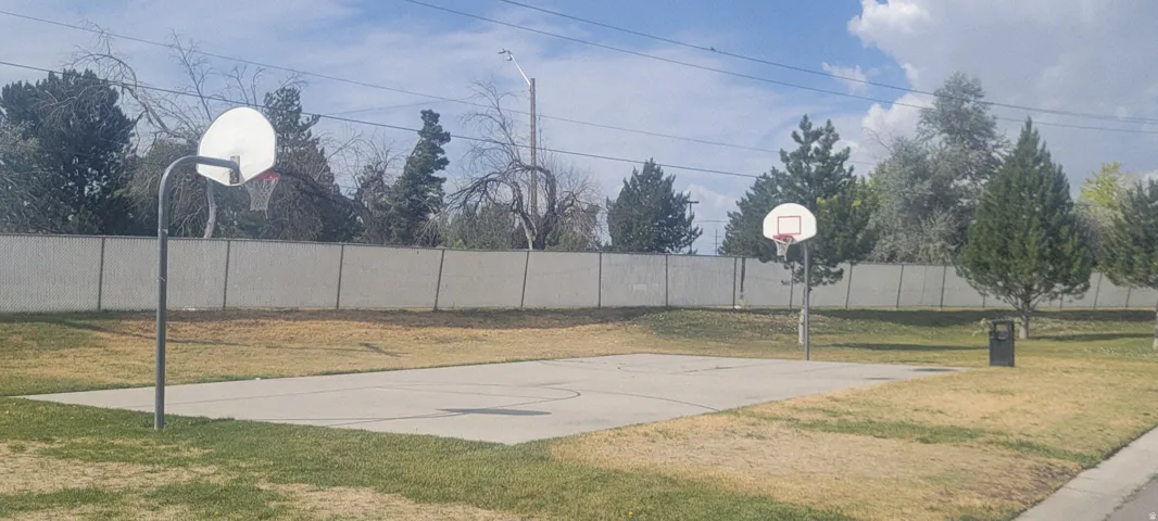 Outdoor recreational court featuring two basketball hoops and a concrete playing surface, surrounded by a chain-link fence