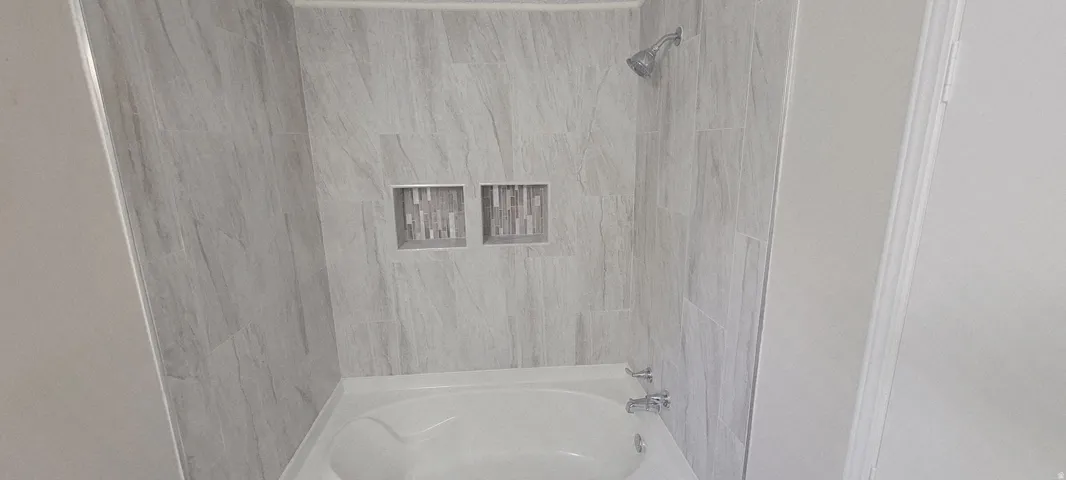 Bathtub and shower combination featuring light gray wall tile with naturalistic veining, two recessed mosaic tile niches, and a chrome showerhead and faucet