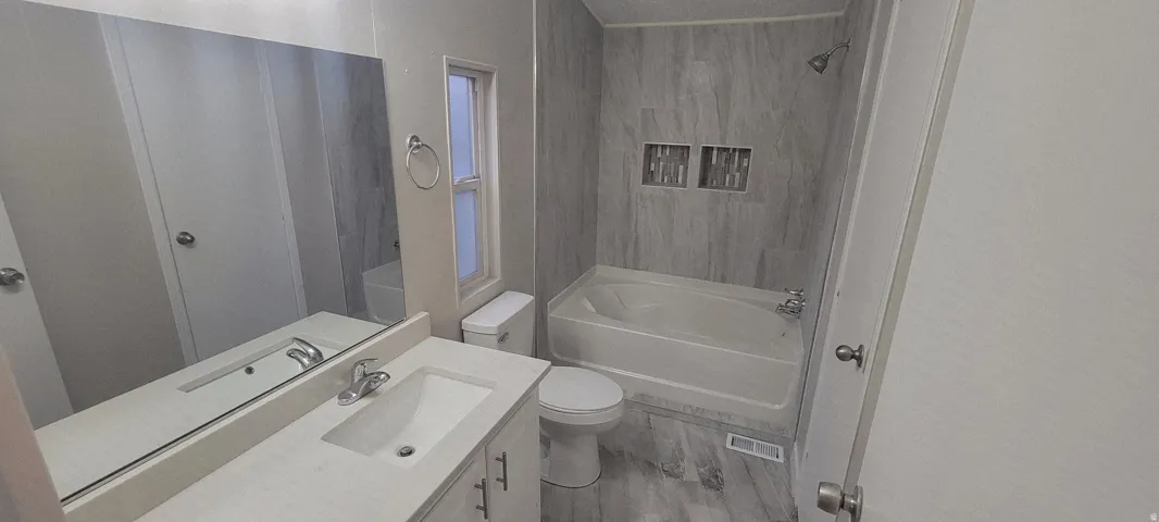 Bathroom featuring a vanity with an integrated sink and chrome faucet, a white bathtub with a shower, and a white toilet