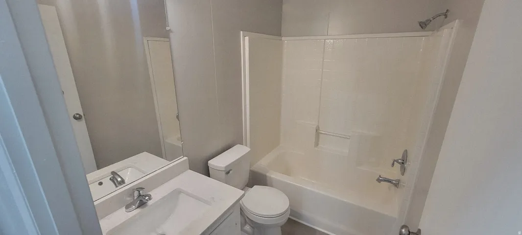 Bathroom featuring a white vanity with an integrated sink, polished chrome faucet, a wall-mounted mirror, white toilet, and a white tub/shower combination with a chrome showerhead