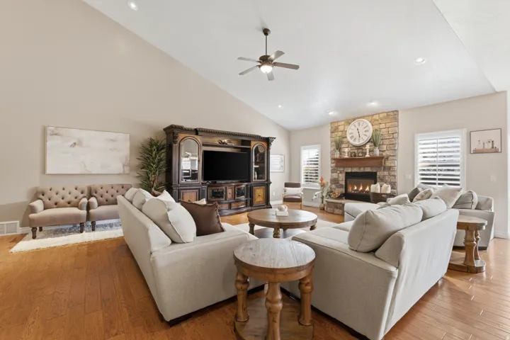 Vaulted ceiling, stone-faced fireplace with wood mantel, wood-finish flooring, ceiling fan, and recessed lighting