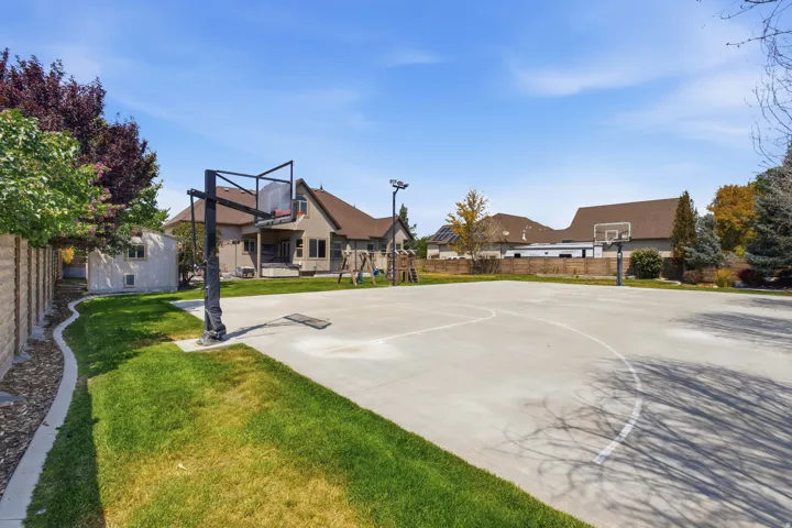 Expansive concrete sports court with two basketball hoops, bordered by a manicured lawn and a block retaining wall