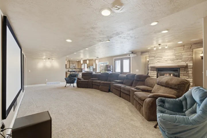 Large projection screen, recessed ceiling lighting, stone-clad fireplace with mantel, double glass doors, and carpeted flooring