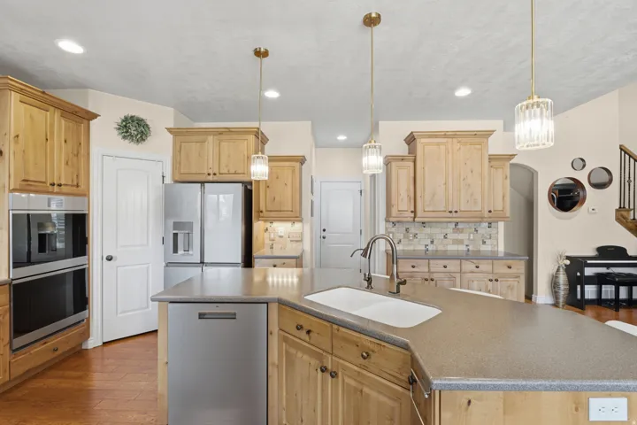 Kitchen with a large island, double wall ovens, built-in stainless steel refrigerator, wood-finish cabinetry, and pendant lighting