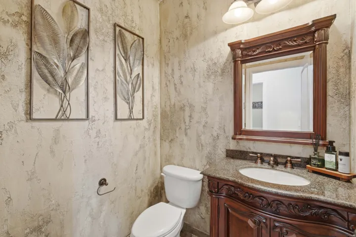 Powder room featuring a carved wood vanity, granite countertop, undermount sink, and ornate framed mirror