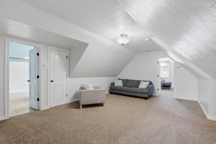 Expansive carpeted area with vaulted ceilings, a built-in light fixture, and white painted walls