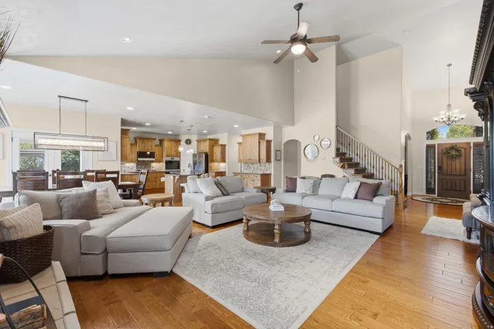 Open-concept living area with vaulted ceilings, hardwood flooring, a staircase with wood treads and white risers, a modern linear chandelier, and a wood entry door with sidelights