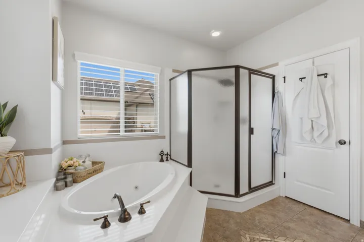 Built-in soaking tub with bronze-tone fixtures, corner shower enclosure with frosted glass, and tile flooring
