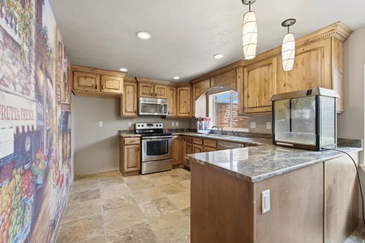 Kitchen featuring wood cabinetry, stainless steel appliances, granite-style countertops, and tile flooring