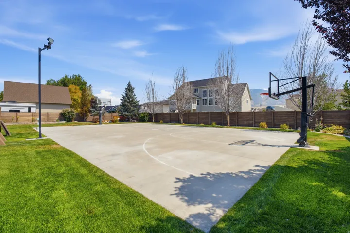 Expansive concrete sports court with two basketball hoops and perimeter lighting, set within a manicured lawn area
