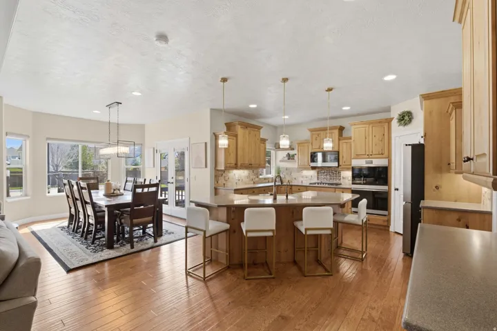 Open-concept kitchen and dining area featuring wood-finish flooring, light-toned cabinetry, stainless steel appliances, a kitchen island with seating, and a built-in oven