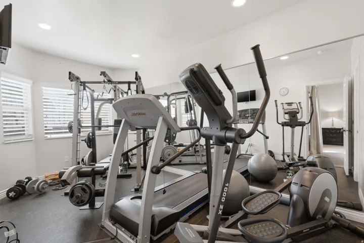 Recessed lighting illuminates a dedicated fitness space featuring durable rubber flooring, mirrored wall accents, and multiple windows with horizontal blinds