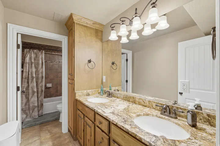 Double vanity with light-colored stone countertop, wood-finish cabinetry, and an integrated tall storage cabinet
