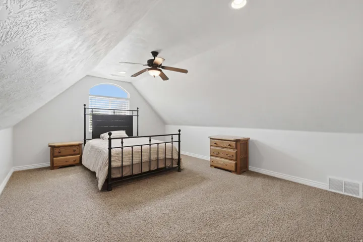 Vaulted ceiling, arched window with horizontal blinds, neutral carpet flooring, recessed lighting, and a ceiling fan with integrated lighting
