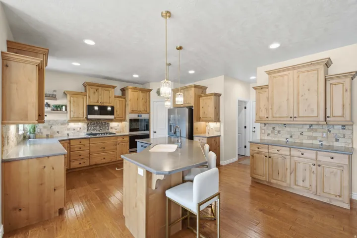 Kitchen featuring extensive wood cabinetry, wood-finish flooring, recessed lighting, a center island with sink, and a tile backsplash