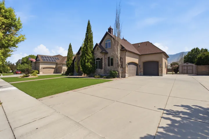 Striking two-story residence featuring a stone and stucco exterior with peaked roofline, circular driveway, and three-car garage