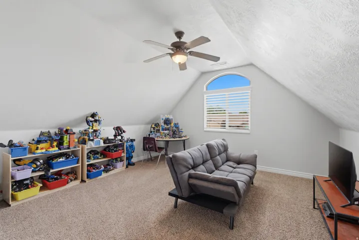 Carpeted room featuring a ceiling fan, sloped ceilings, and an arched window with blinds