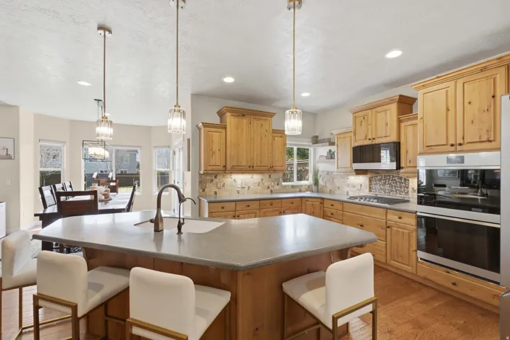 Kitchen featuring warm wood cabinetry, built-in double ovens, a central island with a sink, and pendant lighting