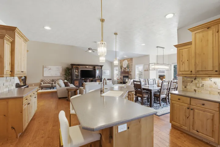Open-concept living space featuring wood-finish flooring, vaulted ceilings, recessed lighting, a stone-faced fireplace, and built-in cabinetry