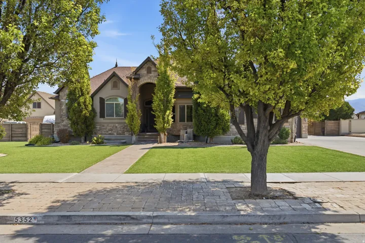 Stone and stucco exterior featuring an arched entryway, established landscaping, a concrete pathway, and a paver sidewalk
