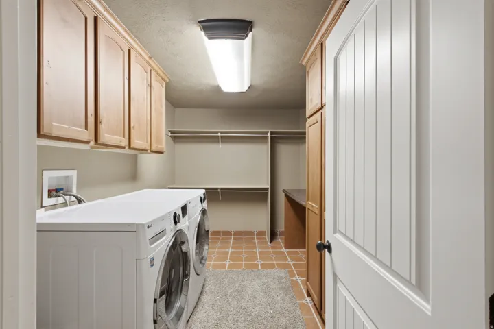Wood-finish upper cabinetry, built-in shelving, tiled flooring, and a solid white door with a dark knob
