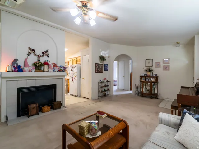 Living area featuring a fireplace with a tiled surround and mantel, a ceiling fan with integrated lighting, and carpet flooring