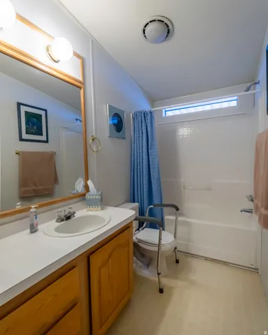 Bathroom featuring a single vanity with wood-finish cabinetry and a white countertop, a drop-in sink with a chrome faucet, a large mirror with a wood-finish frame, and a white bathtub with a shower