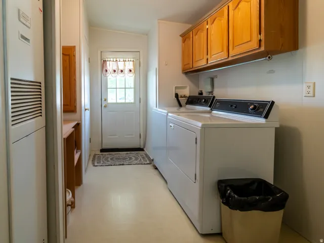 Dedicated laundry area featuring a white washer and dryer set, wood-finish upper cabinetry, and light-toned flooring