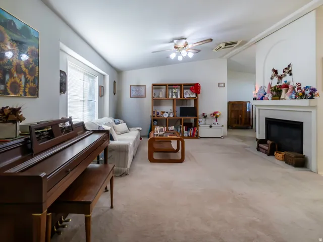 Spacious living area featuring neutral carpeting, a fireplace with mantel, and vaulted ceilings