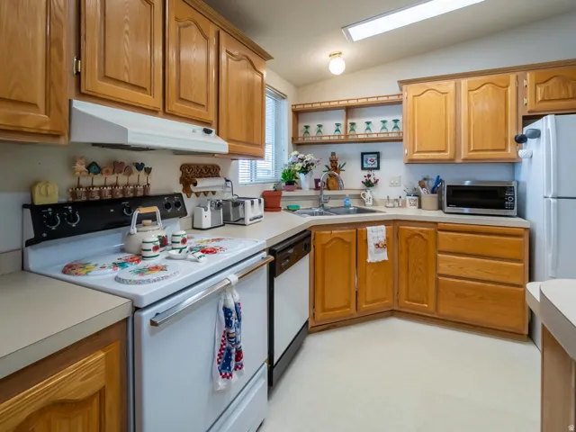 Kitchen featuring wood cabinetry, laminate countertops, a built-in oven with range hood, a double basin sink, and a window with blinds