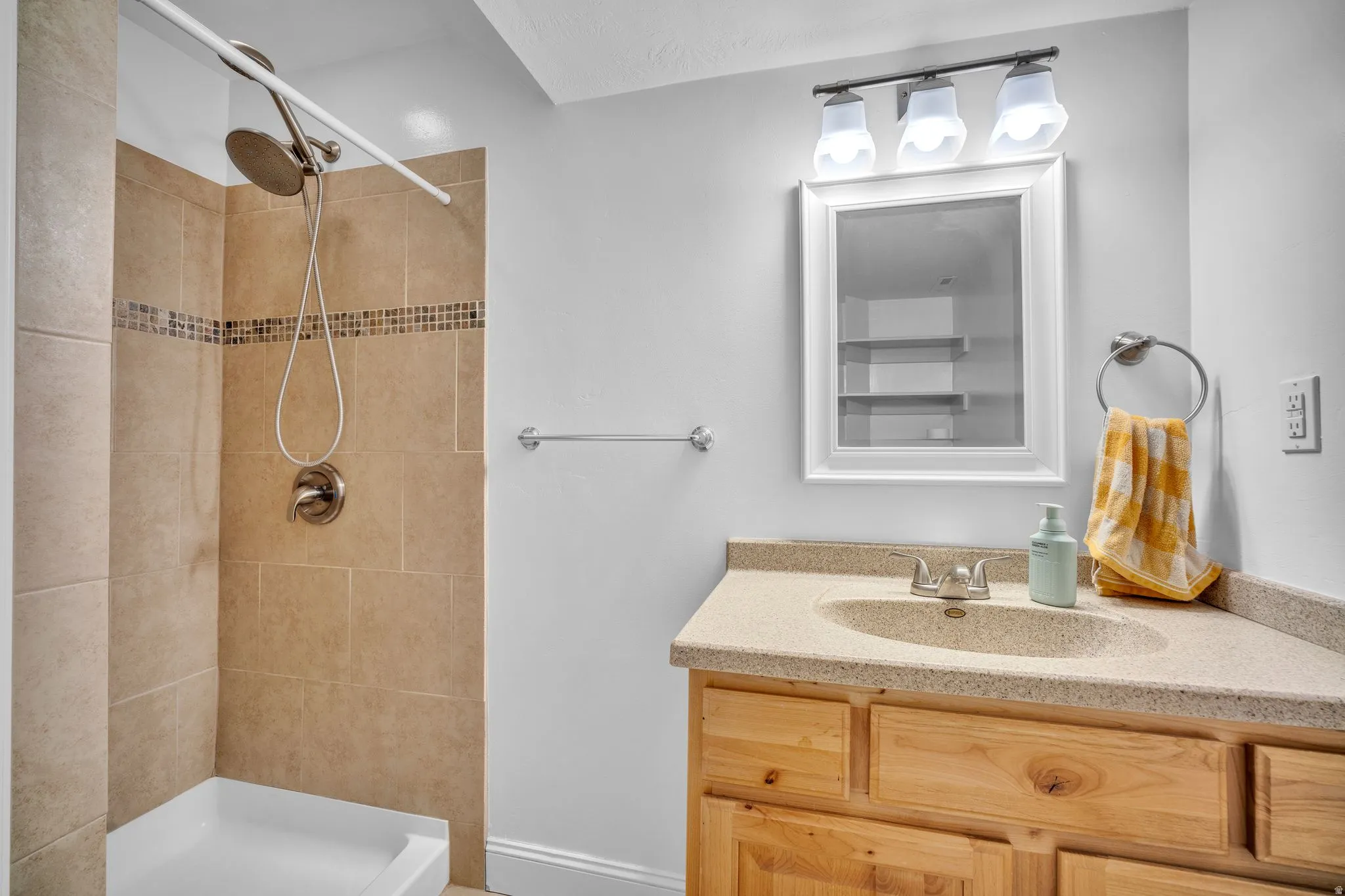 Bathroom featuring a light wood-finish vanity with a built-in sink, a wall-mounted medicine cabinet, and a tiled shower with a mosaic accent band