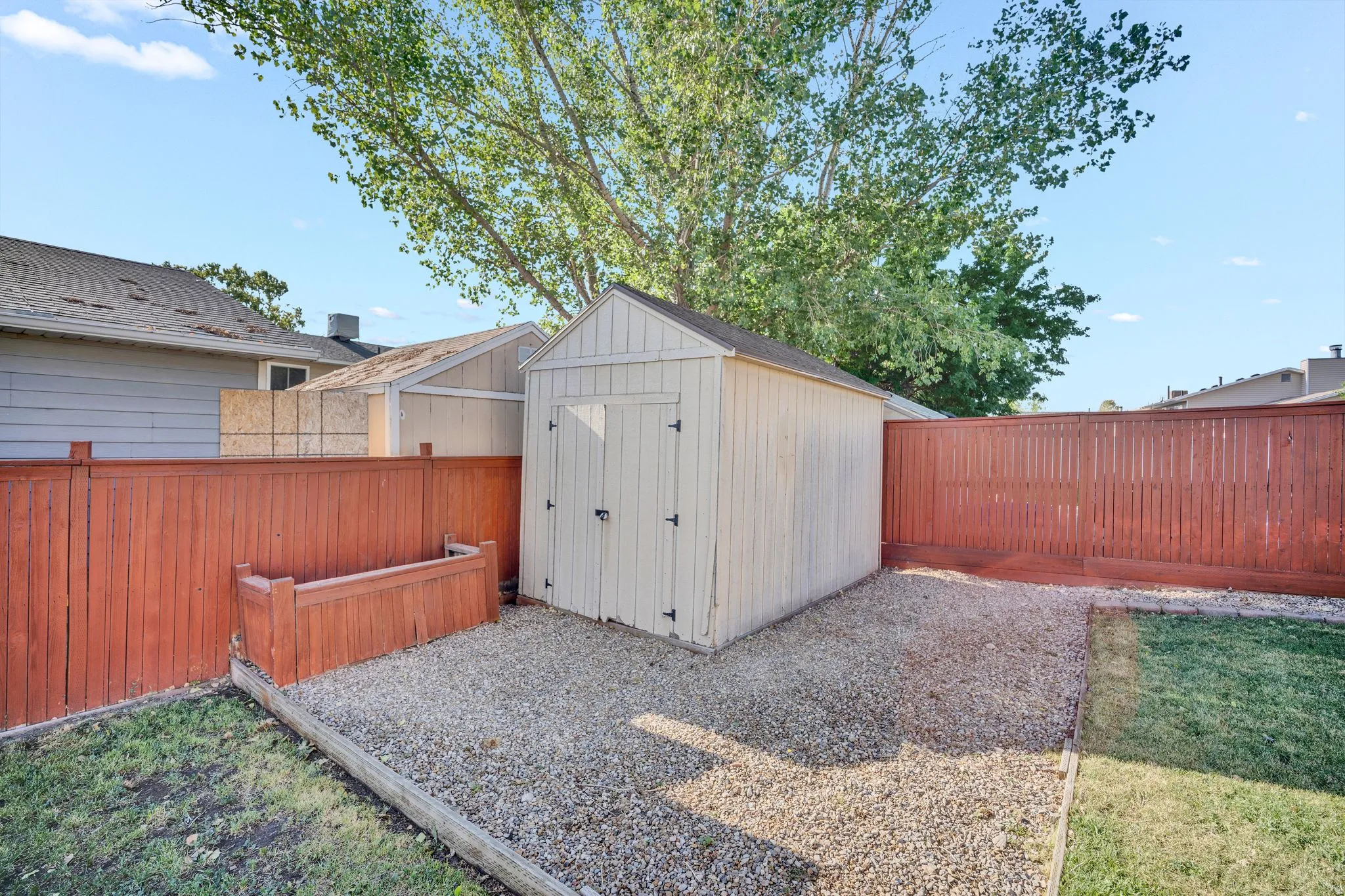 Backyard area featuring a detached storage shed, privacy fencing, gravel ground cover, and a strip of lawn