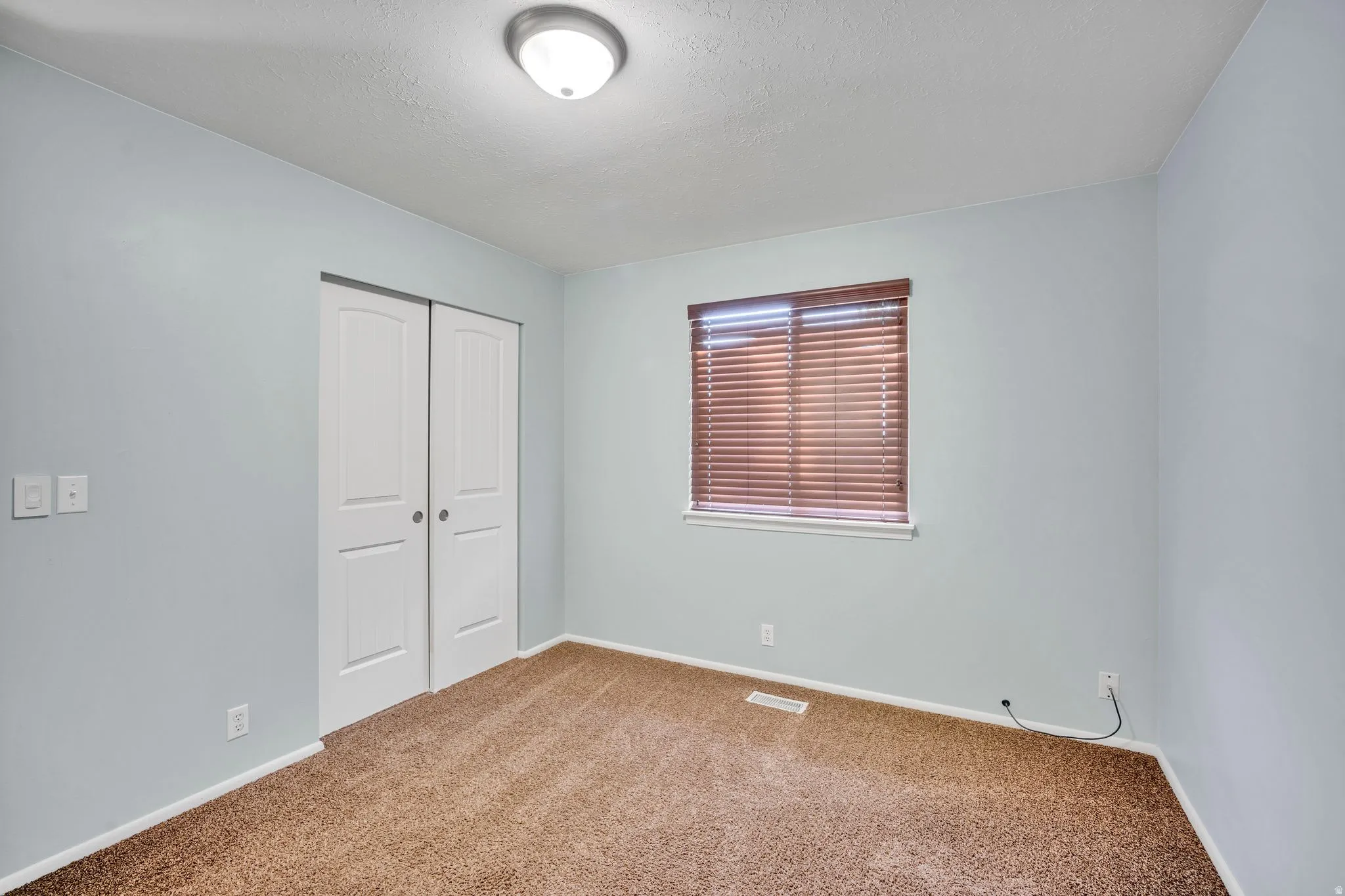 Carpeted room featuring a double-door closet, single window with blinds, and flush-mount ceiling light