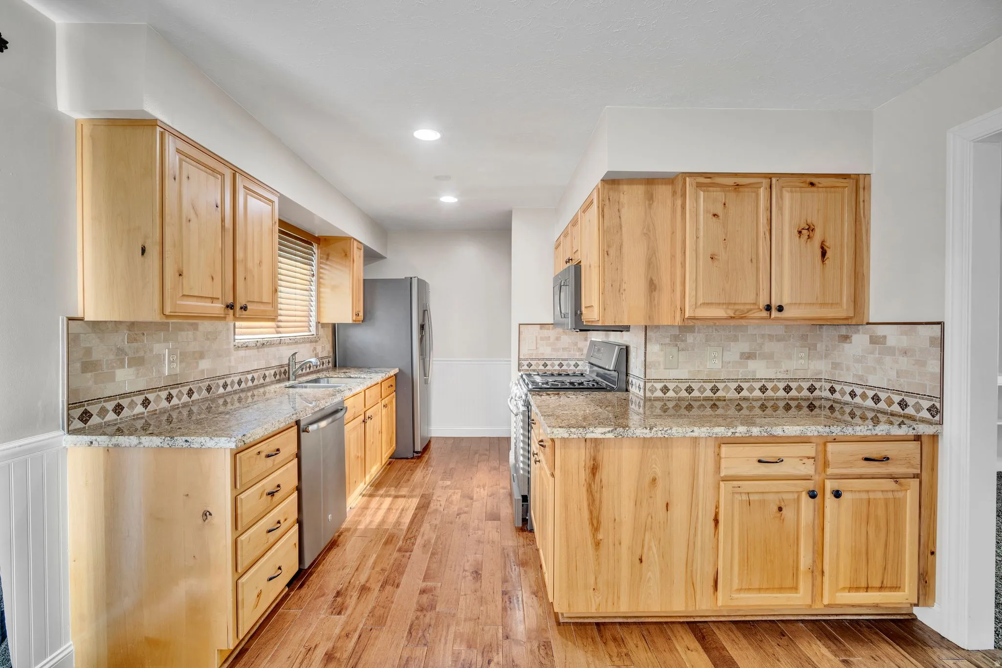 Kitchen featuring light wood cabinetry, stone-finish countertops, stainless steel appliances, and wood-finish flooring