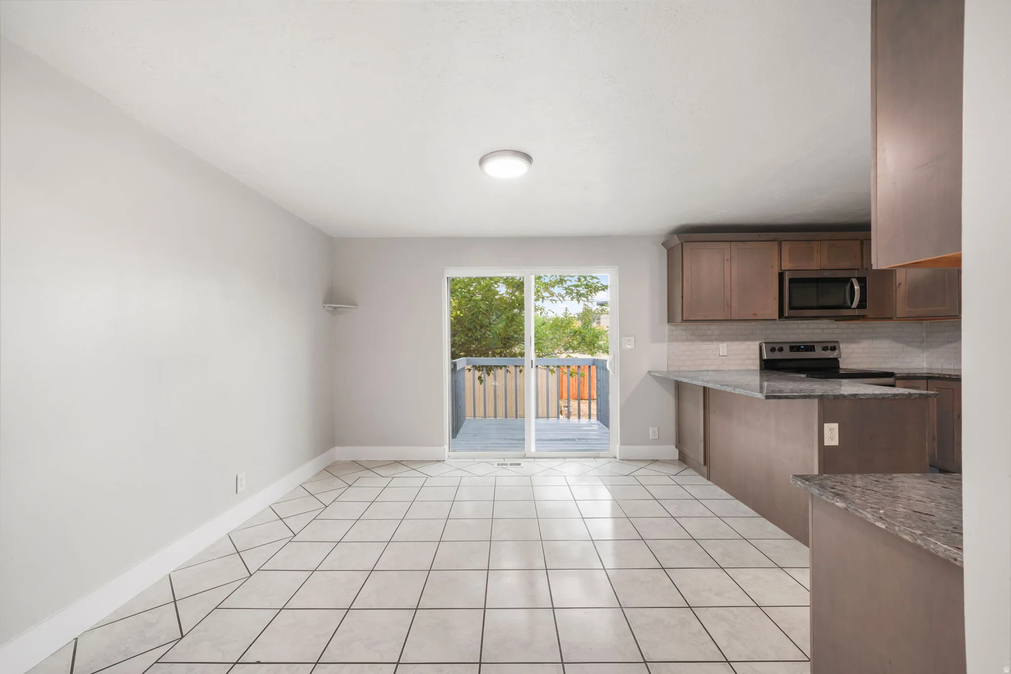 Open concept living area featuring tile flooring, a kitchen with granite-look countertops and wood-finish cabinetry, and a glass slider opening to an outdoor deck