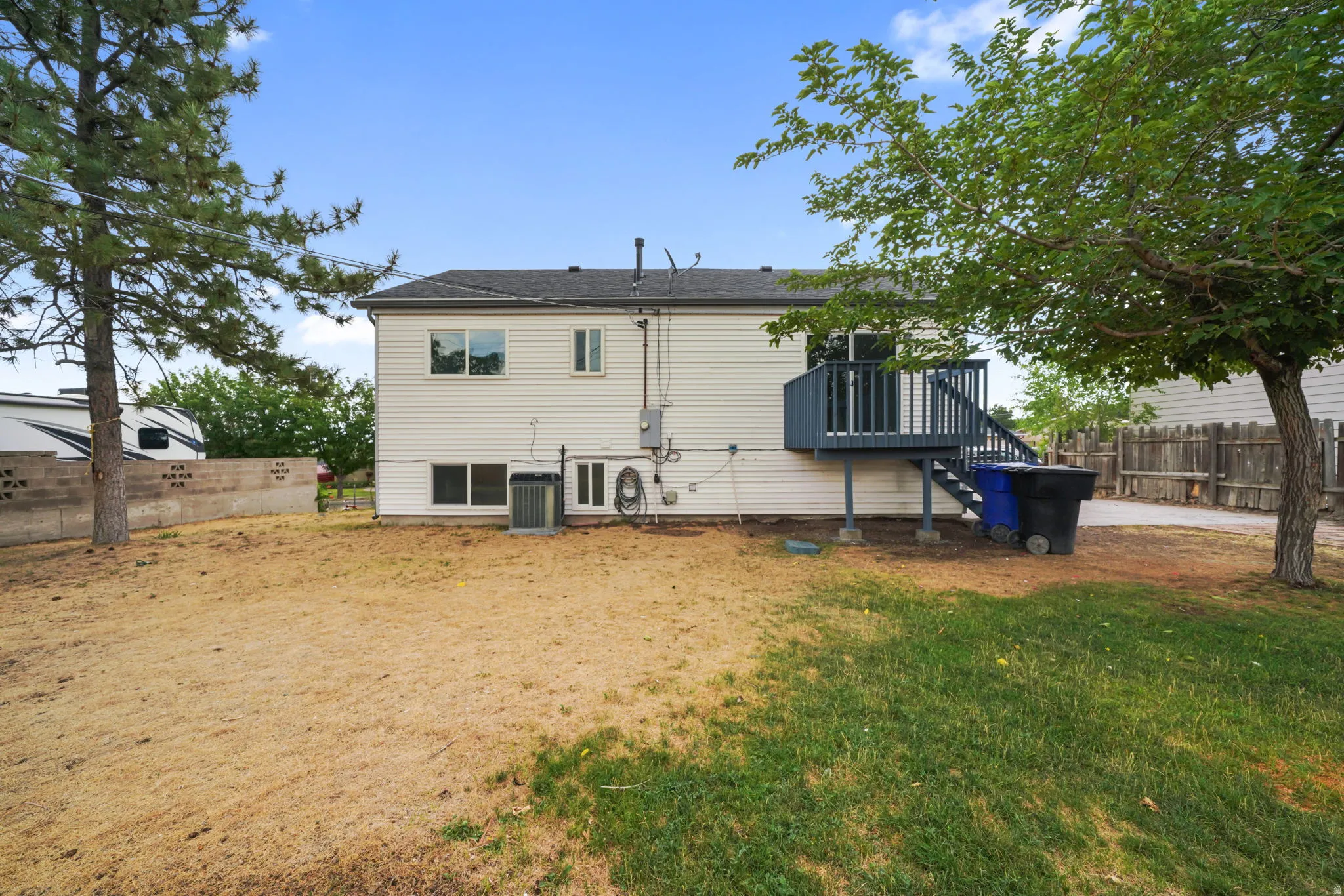 Expansive backyard featuring a partial privacy fence, mature trees, and a raised wooden deck with stairs