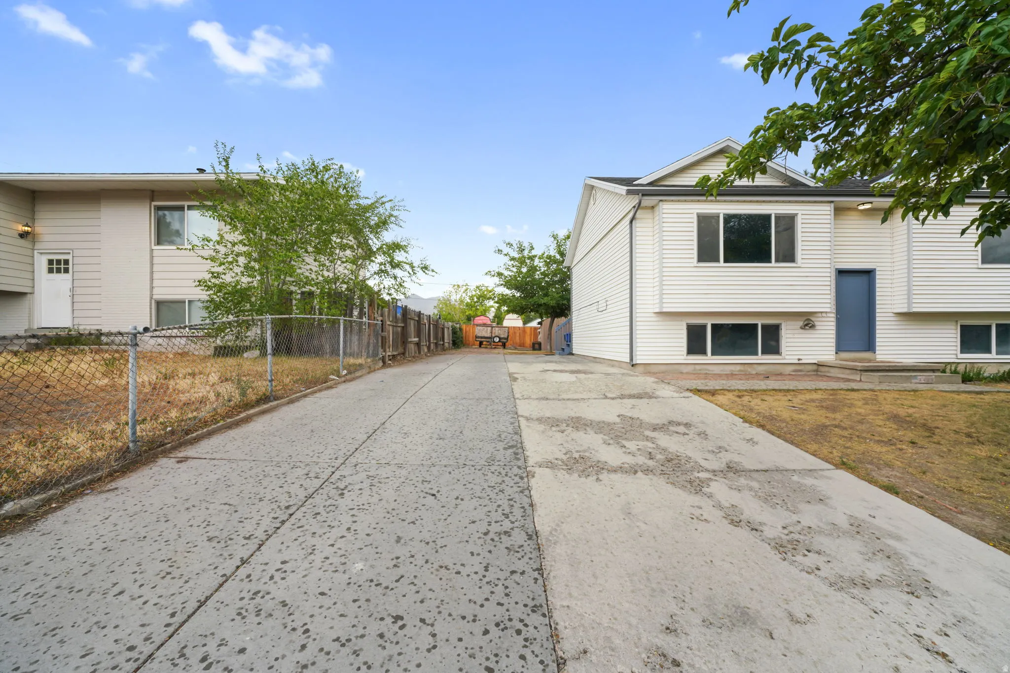 Concrete driveway leading to a white siding residence with a blue entry door