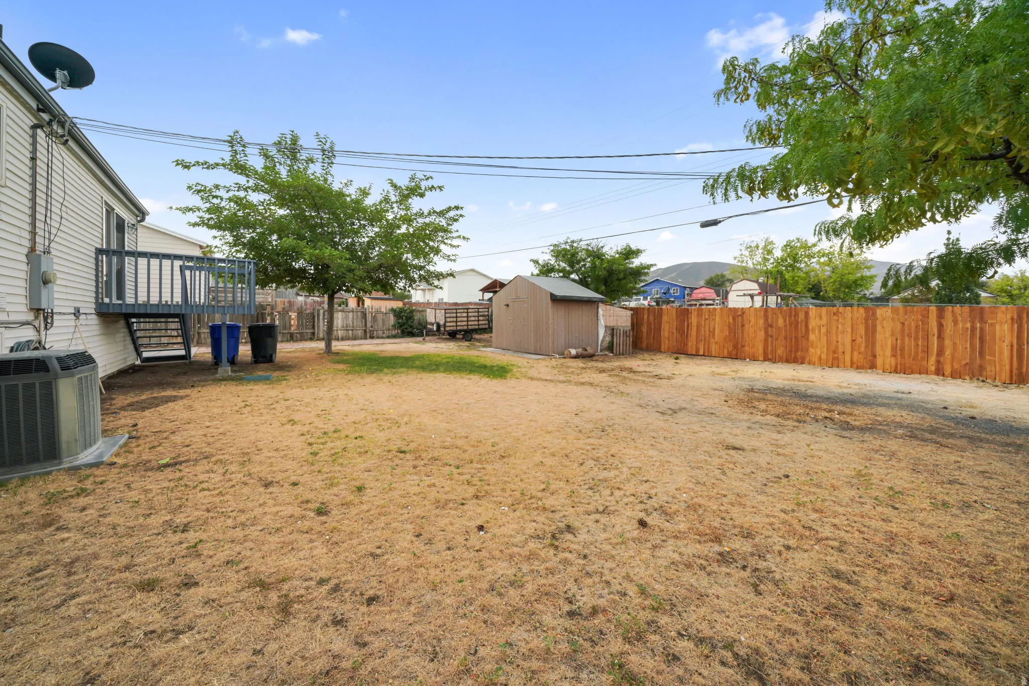 Large backyard with a newly installed wood fence, featuring a raised deck with railing, mature trees, and a detached storage shed