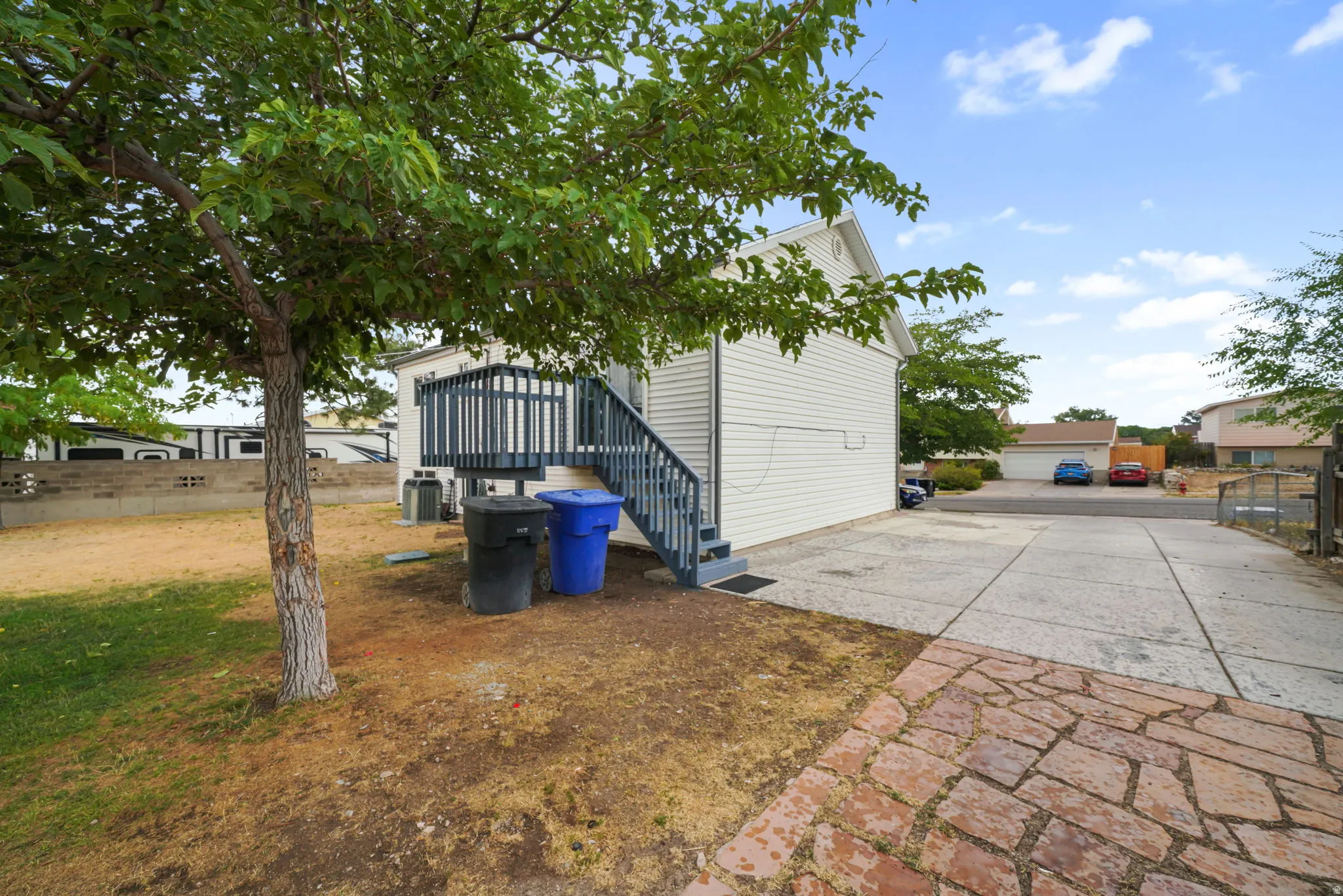 Exterior featuring white siding, a raised deck with dark railing and stairs, and a concrete driveway