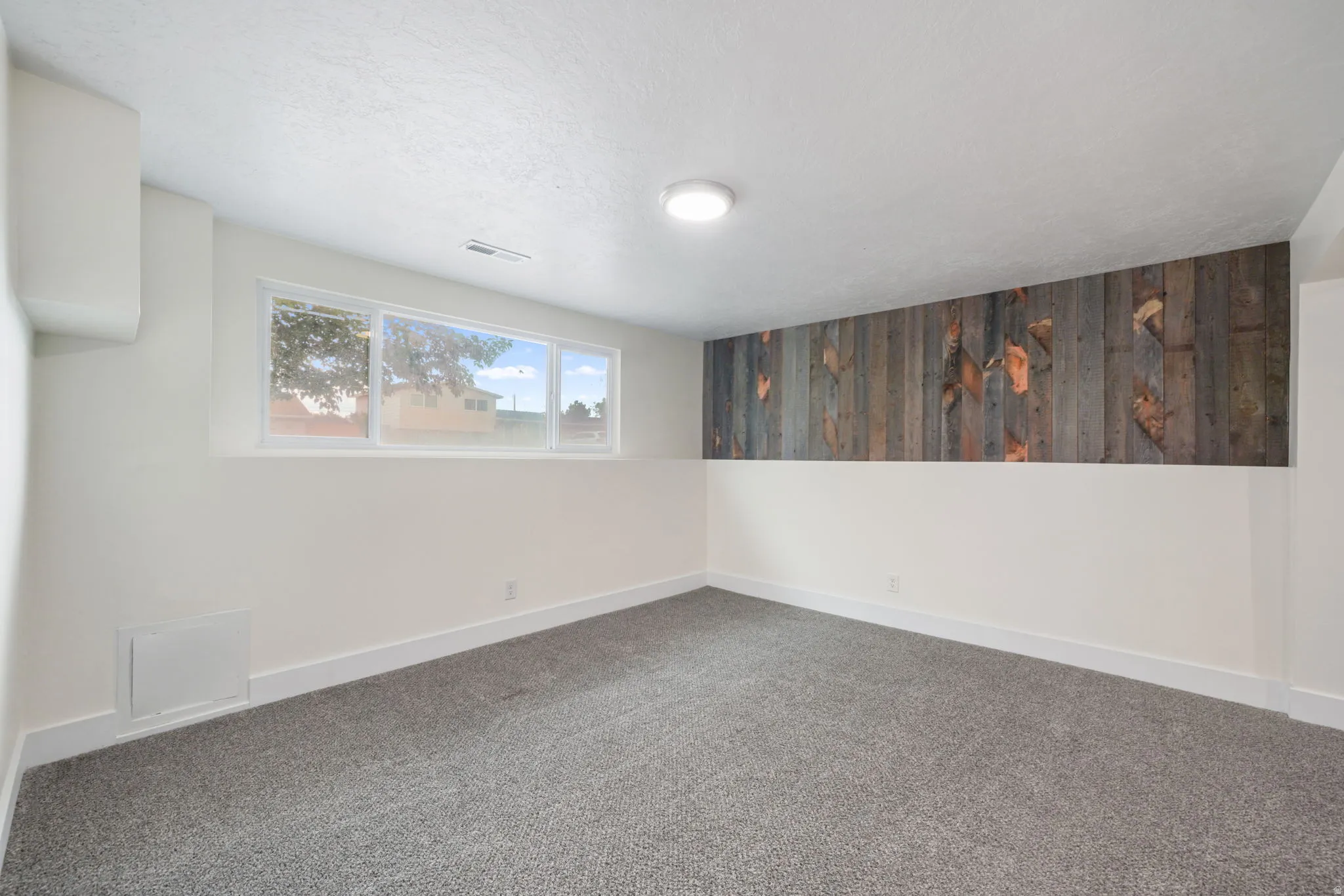 Room featuring a multi-pane window, wood-paneled accent wall, and textured carpeting