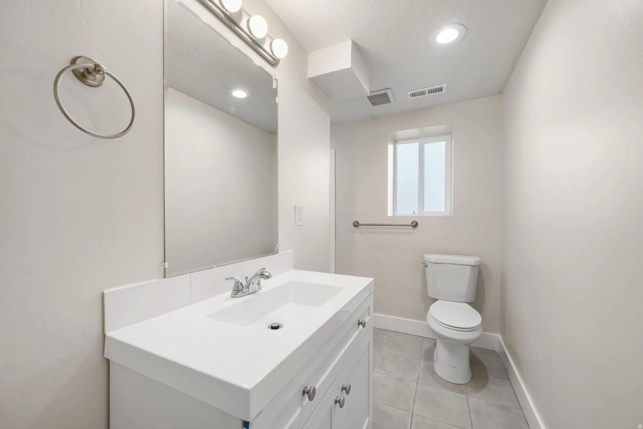 Bathroom featuring a white vanity with integrated sink, chrome faucet, and rectangular mirror