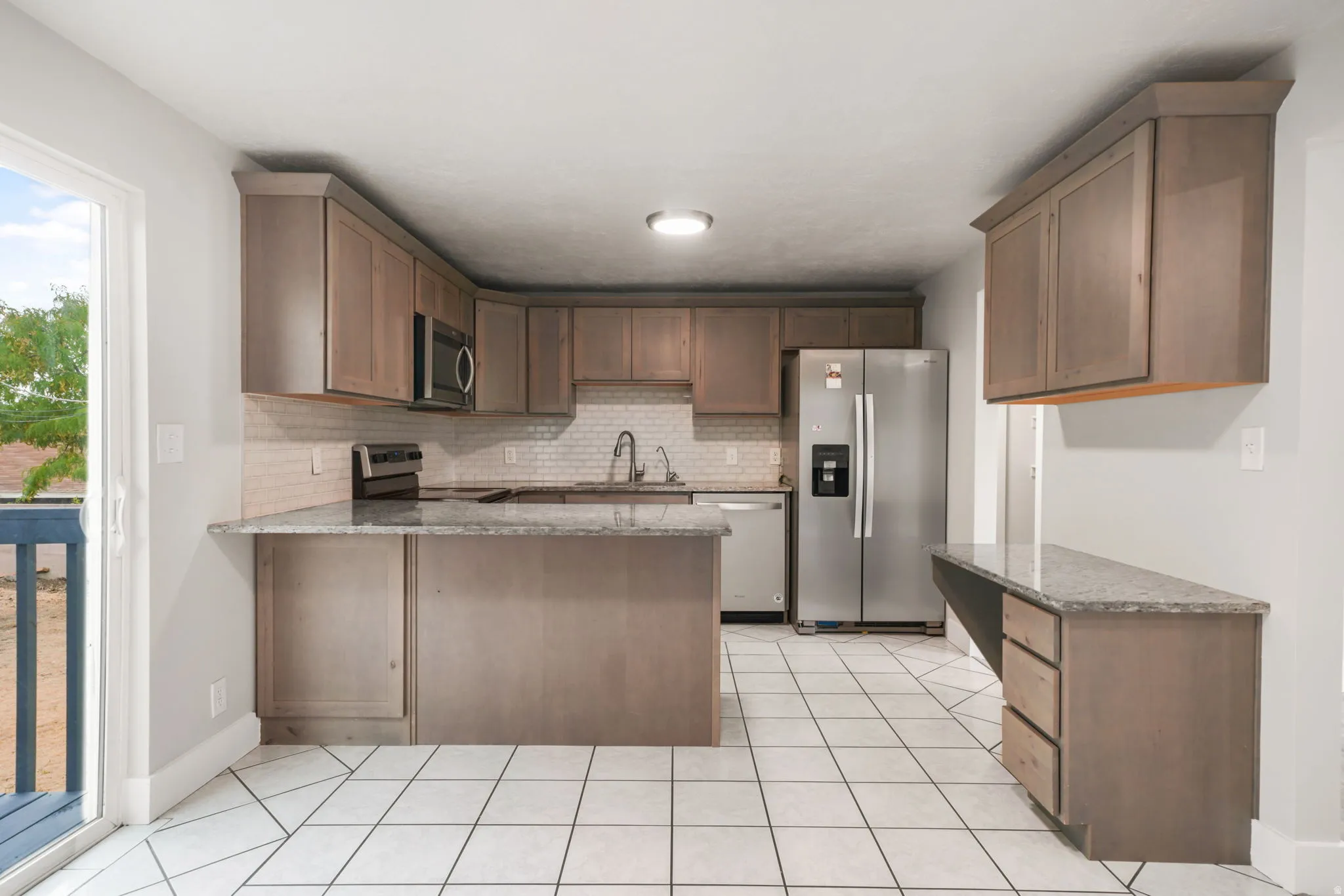 Kitchen featuring light wood-finish cabinetry, granite-style countertops, stainless steel appliances, and a full tile backsplash