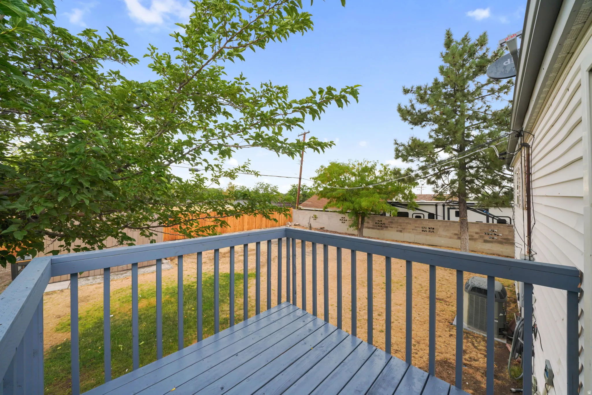 Wood-plank deck featuring a gray finish and railing, overlooking a partially fenced yard with mature trees