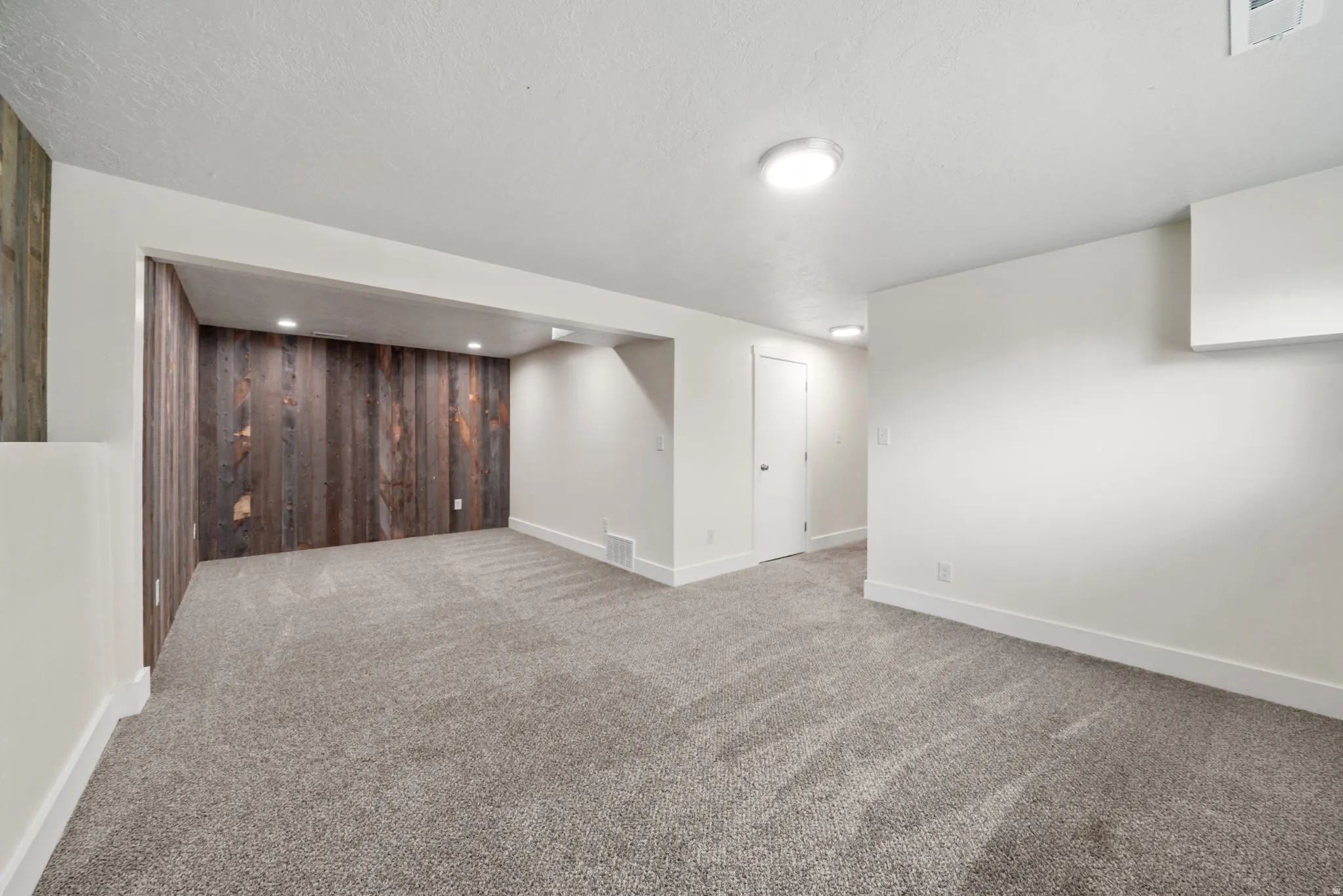 Spacious carpeted room featuring a wood-panel accent wall with recessed lighting, white painted walls, and contemporary flush-mount ceiling lights